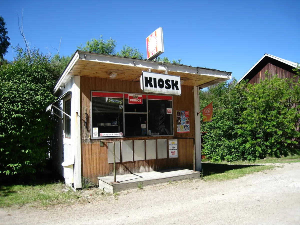 Alter Holzkiosk mit Schild «KIOSK» unter blauem Himmel, davor ein leerer Holzsteg