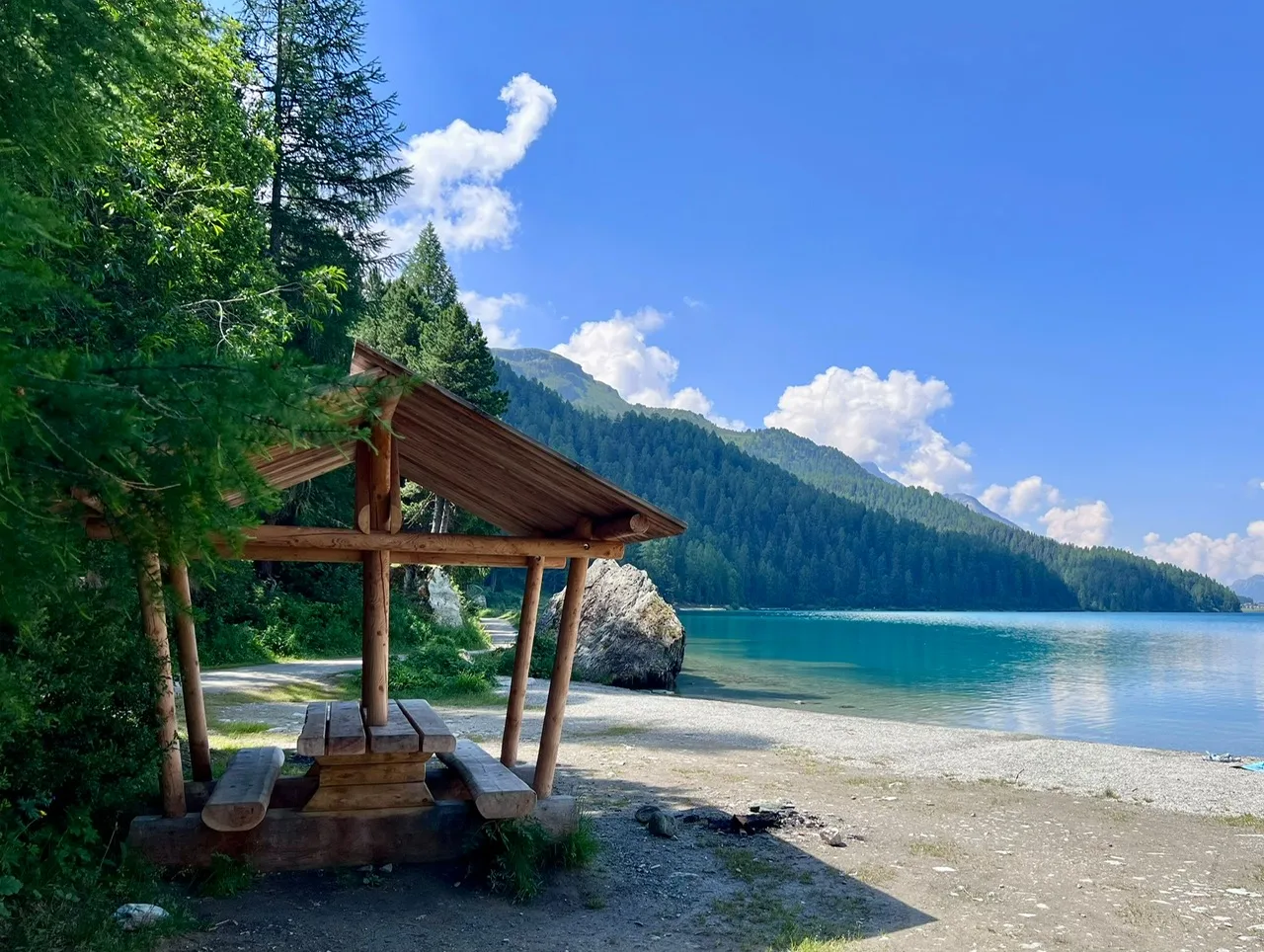 Hölzerner Pavillon mit Sitzbank an einem ruhigen Bergsee, umgeben von Nadelbäumen