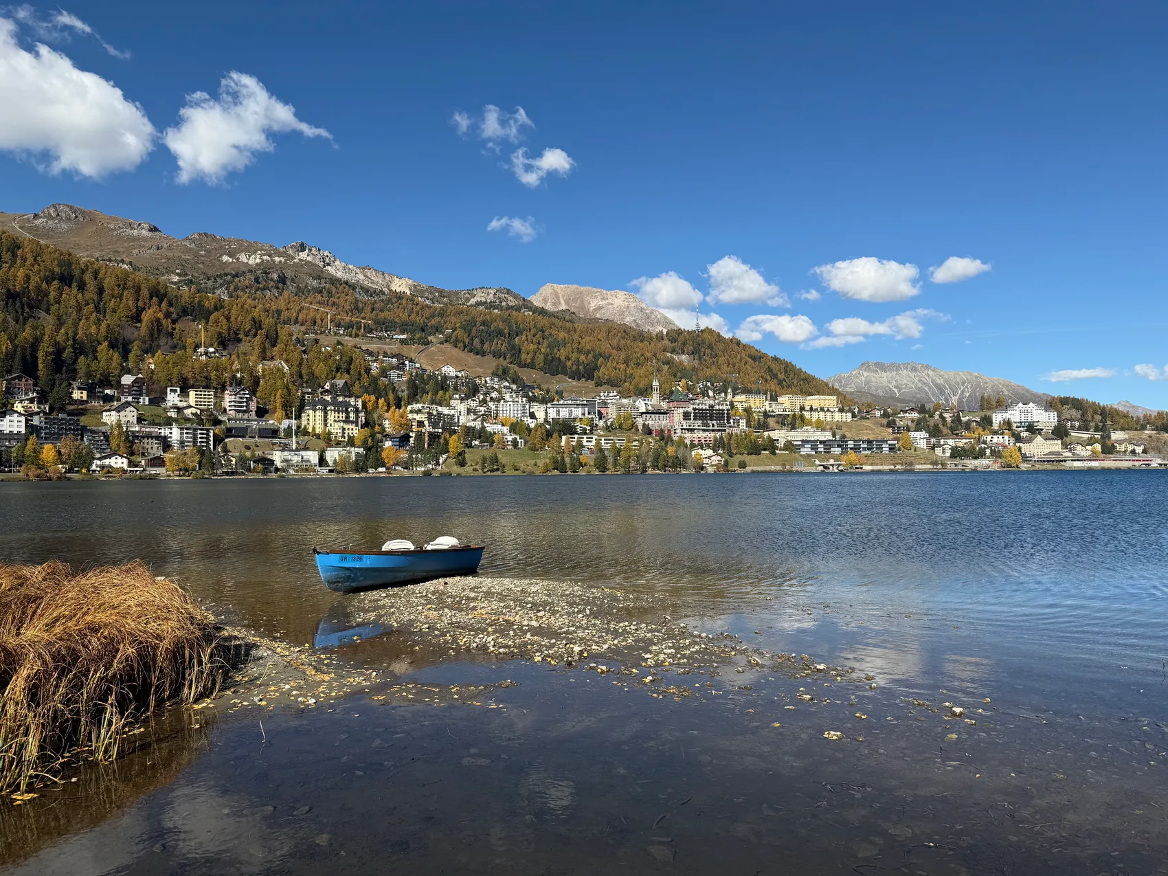 Blaues Ruderboot am Ufer des St. Moritzersees mit Blick auf die Dorfsilhouette im Herbst